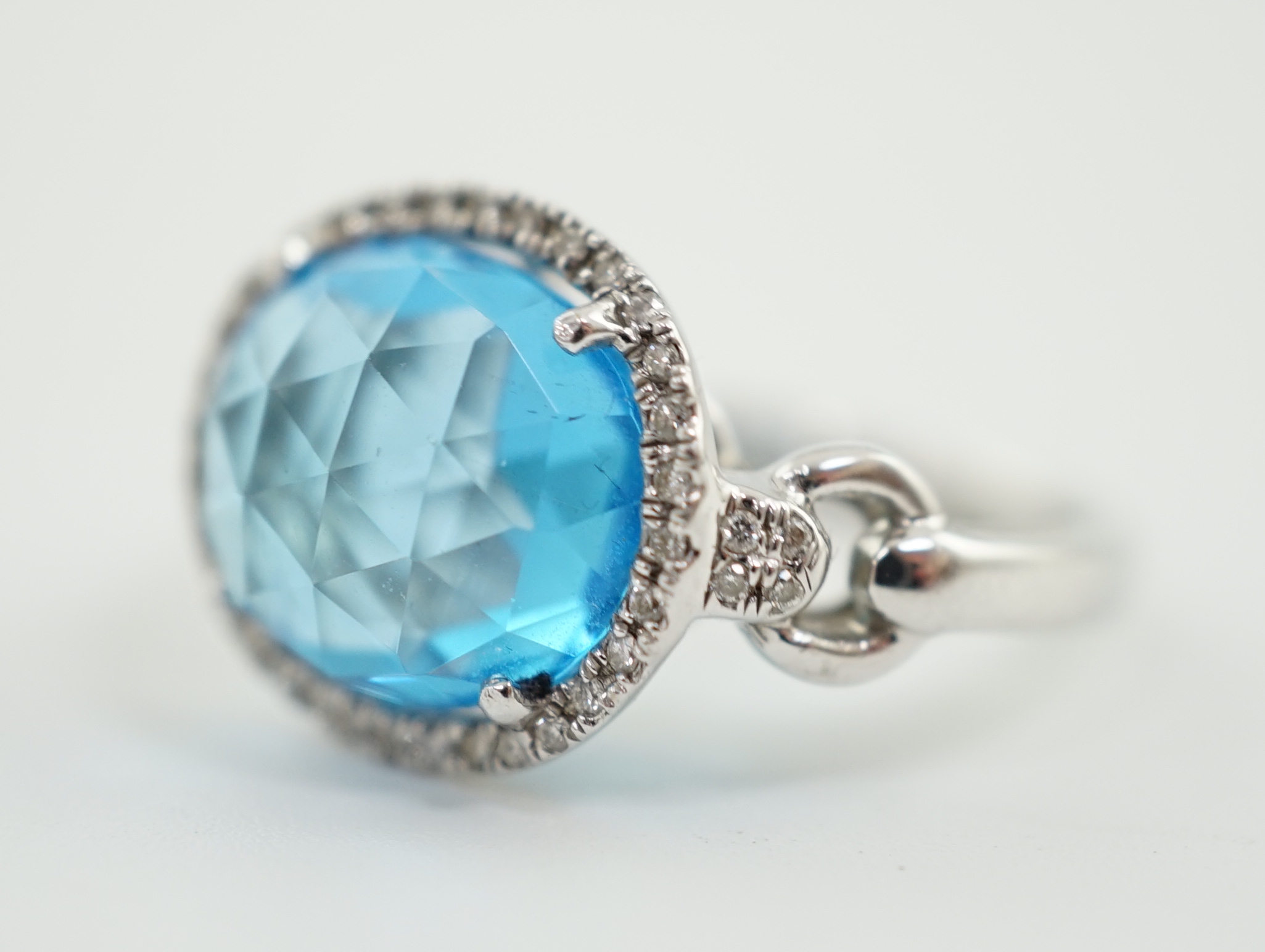 A modern 18ct white gold and facetted oval cut blue topaz set dress ring, with diamond chip set border and shoulders